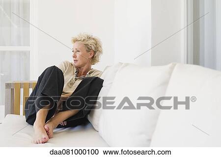 Mature woman sitting on sofa, looking away in thought View Large Photo Image Stock Image - Mature woman sitting on sofa, looking away in thought. Fotosearch
