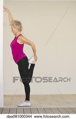 Picture - Mature woman stretching against wall, side view. Fotosearch