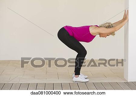 Stock Image - Mature woman stretching against wall, side view. Fotosearch