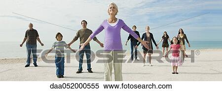 Stock Photography - Mature woman with group of people on beach enjoying fresh sea air. Fotosearch