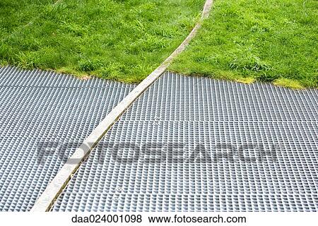 Stock Photo - Metal grate and grass, full frame. Fotosearch