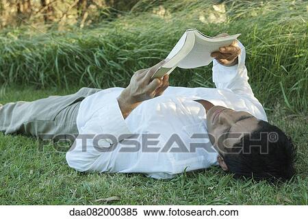 Stock Photography - Mid-adult man lying on grass reading book. Fotosearch
