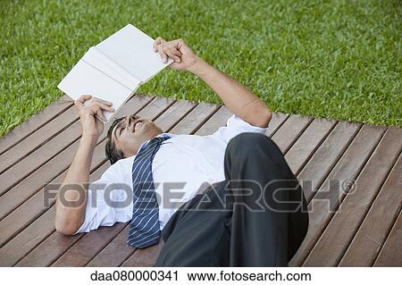 Mid-adult man lying outdoors reading book View Large Photo Image Stock Image - Mid-adult man lying outdoors reading book. Fotosearch