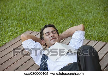 Mid-adult man lying outdoors with hands behind head and book on chest View Large Photo Image Stock Photography - Mid-adult man lying outdoors with hands behind head and book on chest. Fotosearch