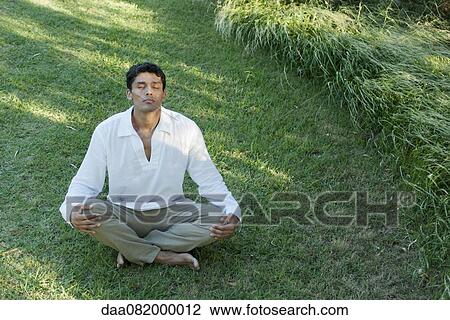 Mid-adult man meditating on grass View Large Photo Image Stock Image - Mid-adult man meditating on grass. Fotosearch