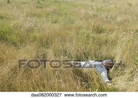 Stock Photo - Mid-adult man relaxing in field with eyes closed. Fotosearch