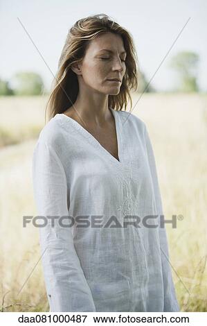 Stock Photo - Mid-adult woman in tunic standing outdoors with eyes closed. Fotosearch
