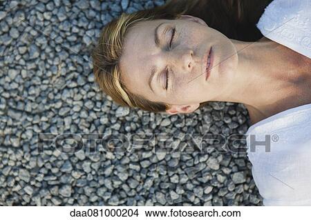 Mid-adult woman lying on gravel with eyes closed, cropped View Large Photo Image Picture - Mid-adult woman lying on gravel with eyes closed, cropped. Fotosearch
