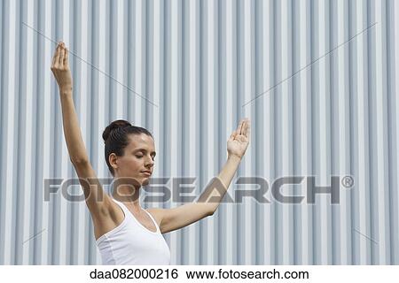 Stock Photograph - Mid-adult woman meditating outdoors with eyes closed and arms raised. Fotosearch