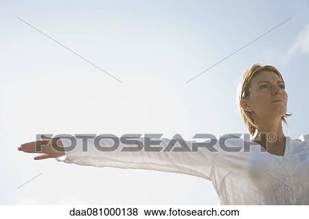 Stock Photo - Mid-adult woman with arms outstretched outdoors, low angle view. Fotosearch