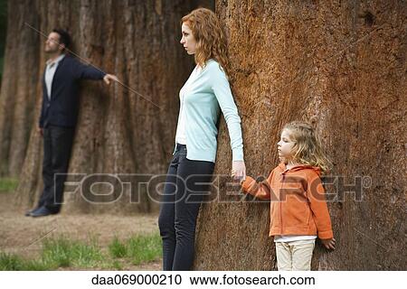Mother and daughter leaning against tree, father standing separate in background View Large Photo Image Stock Image - Mother and daughter leaning against tree, father standing separate in background. Fotosearch