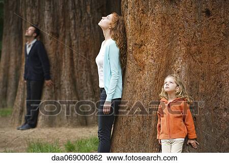 Stock Image - Mother and daughter leaning against tree trunk, breathing fresh air. Fotosearch