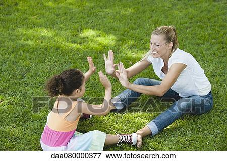 Mother and daughter sitting on grass playing patty-cake View Large Photo Image Stock Photo - Mother and daughter sitting on grass playing patty-cake. Fotosearch