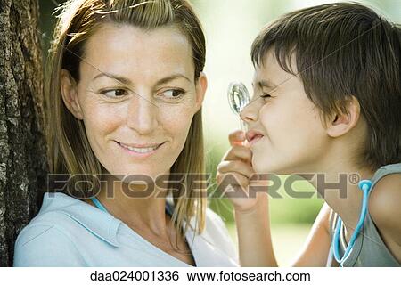 Stock Photograph - Mother and son, boy looking through magnifying glass, close-up. Fotosearch