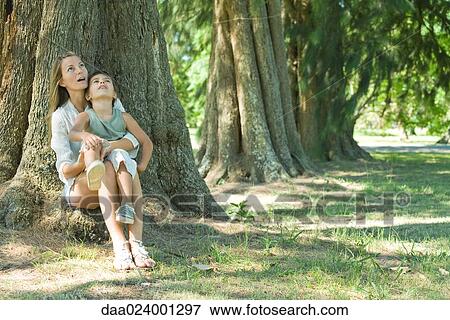 Mother and son, sitting on base of tree, looking up View Large Photo Image Stock Photo - Mother and son, sitting on base of tree, looking up. Fotosearch