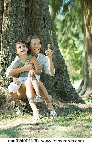 Mother and son, sitting on base of tree, looking out of frame View Large Photo Image Stock Photo - Mother and son, sitting on base of tree, looking out of frame. Fotosearch