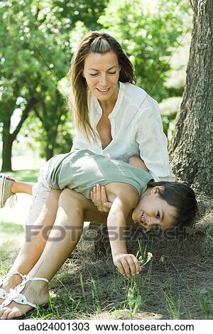 Mother and son, sitting on ground, boy on woman's lap, reaching for flower View Large Photo Image Stock Image - Mother and son, sitting on ground, boy on woman's lap, reaching for flower. Fotosearch