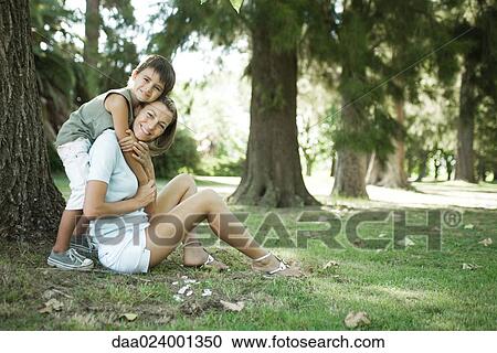 Mother and son sitting outdoors, boy hugging woman from behind View Large Photo Image Stock Image - Mother and son sitting outdoors, boy hugging woman from behind. Fotosearch