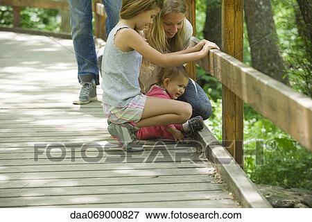 Stock Photo - Mother and two young daughters looking over railing of bridge together. Fotosearch
