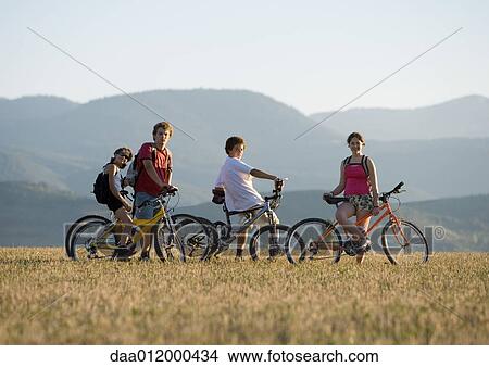 Picture - Mountain bikers stopped in field, mountains in background. Fotosearch
