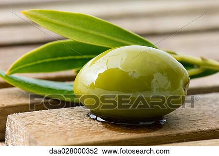 Stock Image - Olive and sprig of leaves on wood table, close-up. Fotosearch