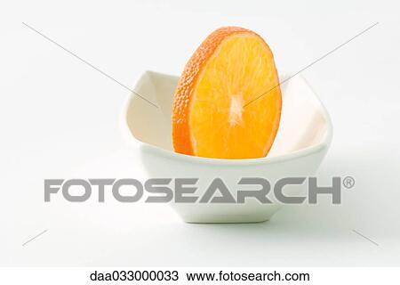 Stock Image - Orange slice in small dish, close-up. Fotosearch