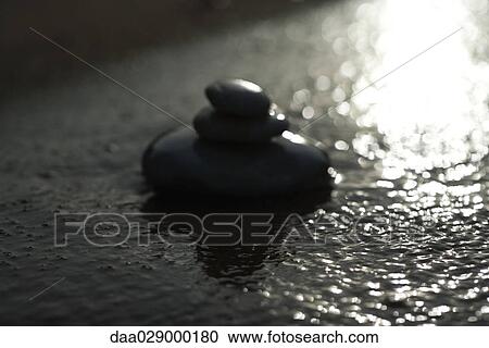 Stock Image - Pebbles stacked in shallow water, close-up. Fotosearch