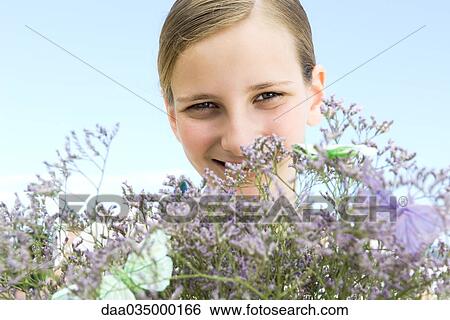 Preteen girl looking over top of flowering plant, smiling at camera View Large Photo Image Stock Photograph - Preteen girl looking over top of flowering plant, smiling at camera. Fotosearch