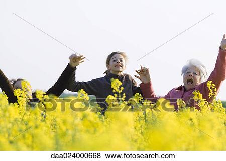 Stock Photo - Senior woman and two granddaughters standing in field, holding hands and jumping into the air. Fotosearch