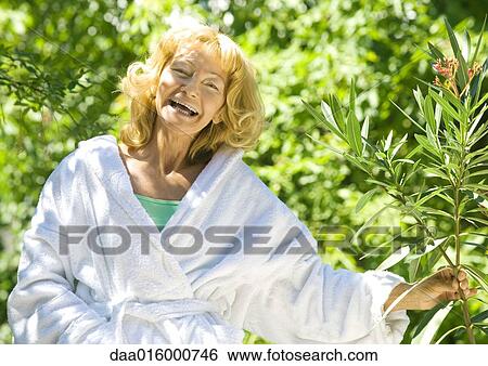 Senior woman in bathrobe holding branch of shrub, laughing View Large Photo Image Stock Photograph - Senior woman in bathrobe holding branch of shrub, laughing. Fotosearch