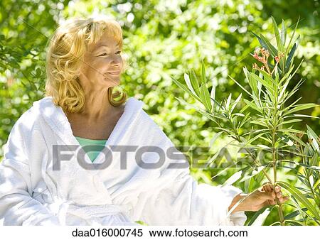 Senior woman in bathrobe smiling and examining branch of shrub View Large Photo Image Stock Photography - Senior woman in bathrobe smiling and examining branch of shrub. Fotosearch