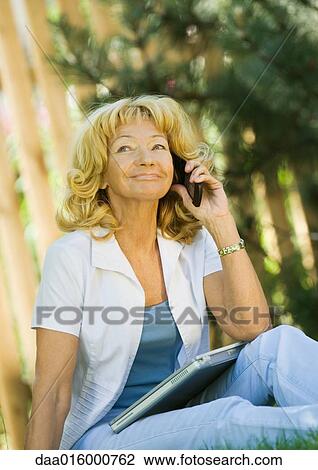 Senior woman sitting outdoors with laptop on lap View Large Photo Image Stock Image - Senior woman sitting outdoors with laptop on lap. Fotosearch