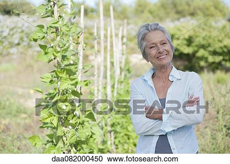Stock Image - Senior woman smiling proudly in vegetable garden. Fotosearch