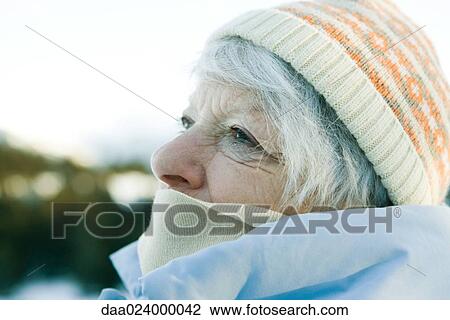 Stock Image - Senior woman wearing knit hat and scarf, looking up, head and shoulders. Fotosearch