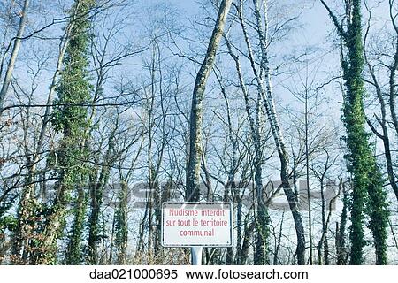 Stock Photography - Sign in front of woods in French stating Nudism forbidden throughout the district. Fotosearch