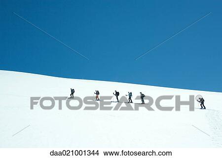 Picture - Skiers going up snowy slope, single file. Fotosearch