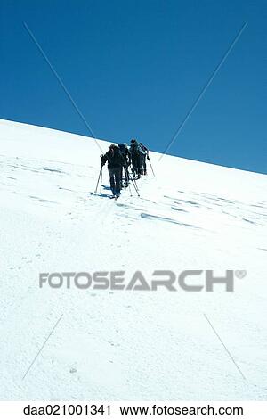Stock Image - Skiers moving up slope, rear view. Fotosearch