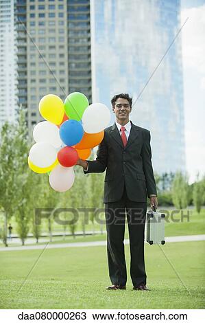 Smiling businessman holding bunch of balloons View Large Photo Image Stock Image - Smiling businessman holding bunch of balloons. Fotosearch