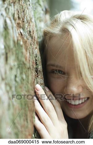 Smiling young woman leaning against tree trunk, cropped View Large Photo Image Stock Photography - Smiling young woman leaning against tree trunk, cropped. Fotosearch