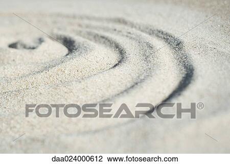 Stock Image - Spiral shape drawn in sand, close-up, surface level. Fotosearch