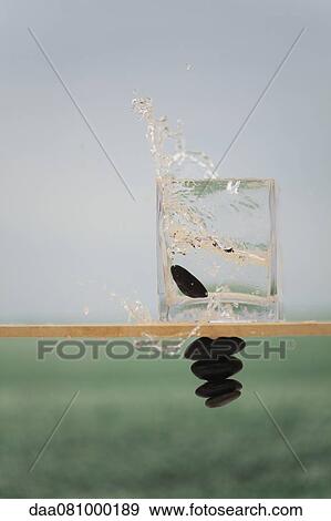 Stone falling in glass container, creating water splash, stack of stones defying gravity View Large Photo Image Stock Photo - Stone falling in glass container, creating water splash, stack of stones defying gravity. Fotosearch