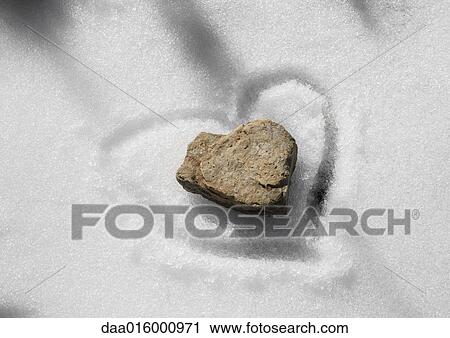 Stock Image - Stone on snow with heart traced around it. Fotosearch