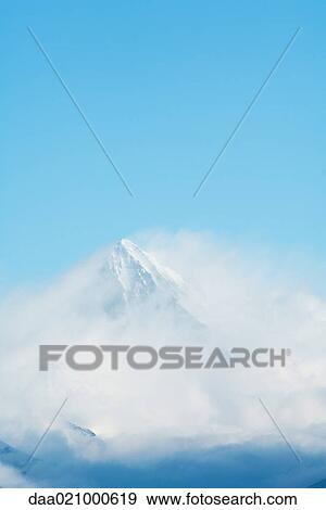 Stock Photo - Switzerland, clouds moving over snowy mountain peak. Fotosearch