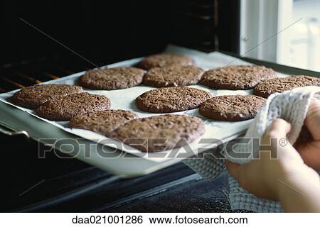 Stock Photograph - Taking sheet of cookies out of the oven. Fotosearch