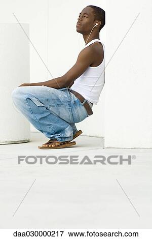 Teen boy crouching, listening to earphones, side view View Large Photo Image Stock Photo - Teen boy crouching, listening to earphones, side view. Fotosearch