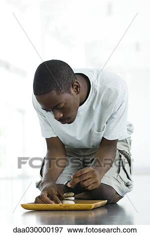 Teen boy crouching on the ground, stacking rocks on tray View Large Photo Image Stock Photo - Teen boy crouching on the ground, stacking rocks on tray. Fotosearch