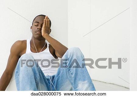 Stock Photography - Teen boy listening to earphones, eyes closed, hand on face. Fotosearch