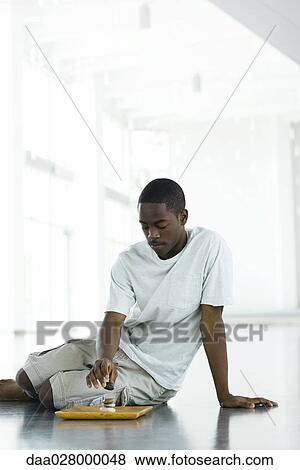 Stock Photo - Teen boy sitting on floor, stacking rocks on tray. Fotosearch