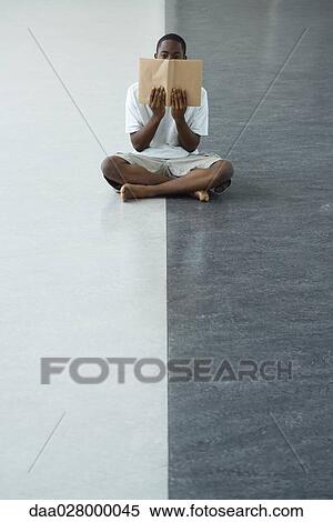 Teen boy sitting on ground, holding up book in front of lower face View Large Photo Image Stock Photography - Teen boy sitting on ground, holding up book in front of lower face. Fotosearch