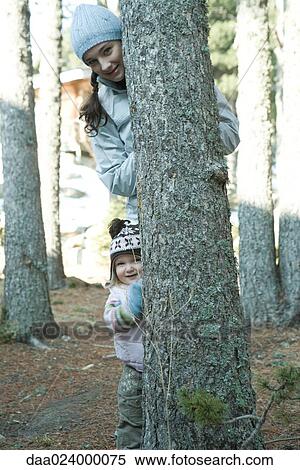 Stock Photography - Teen girl and toddler, peeking out from behind tree trunk. Fotosearch